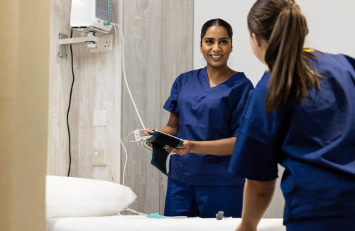 Two female fertility nurses wearing scrubs, chatting to eachother and setting up a patient's room for her fertility treatment