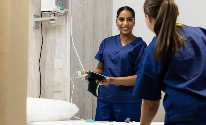 Two female fertility nurses wearing scrubs, chatting to eachother and setting up a patient's room for her fertility treatment
