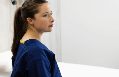 Fertility nurse in scrubs, standing in a treatment room looking into the distance