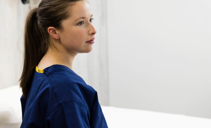 Fertility nurse in scrubs, standing in a treatment room looking into the distance