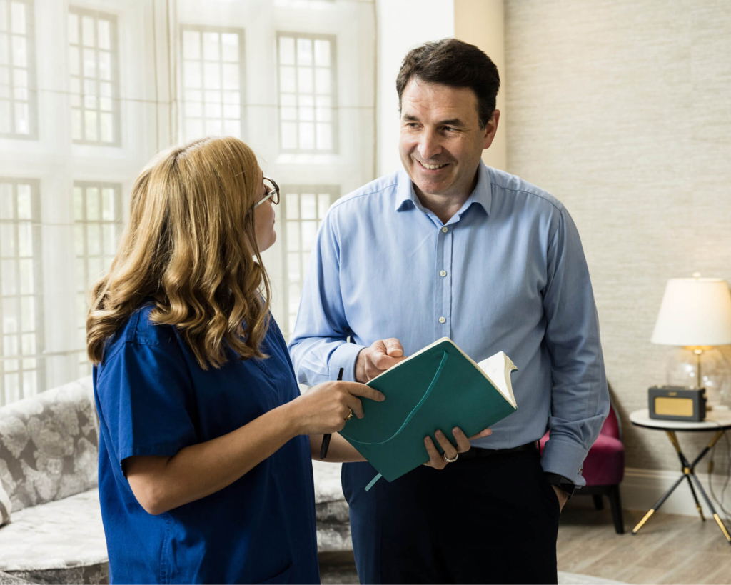 Consultant discussing male fertility looking at an open notebook with an Evewell nurse in blue srubs