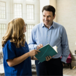 Consultant discussing male fertility looking at an open notebook with an Evewell nurse in blue srubs