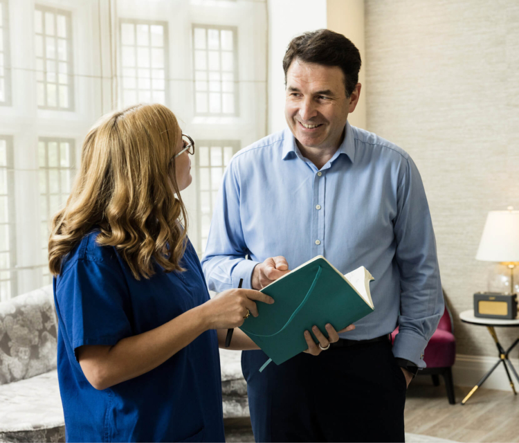 Consultant discussing male fertility looking at an open notebook with an Evewell nurse in blue srubs